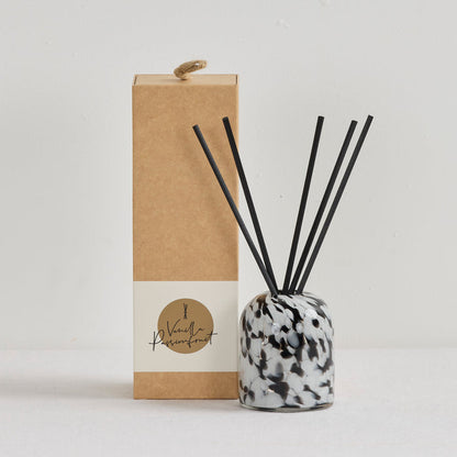 Aurora Diffuser - Vanilla Passionfruit reed diffuser in a mottled black, white and grey vessel with black reeds beside kraft gift box