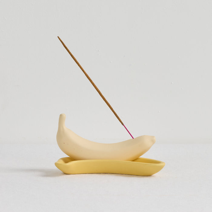 Yellow ceramic incense holder with a single incense stick on a light gray background