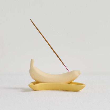 Yellow ceramic incense holder with a single incense stick on a light gray background