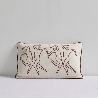 A rectangular cream-colored throw pillow with a dark brown border and embroidered line art of four dancing figures, set against a neutral light gray background.
