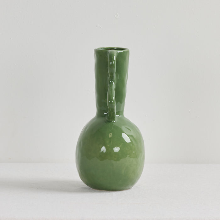 Green ceramic vase with a handle on a light gray background