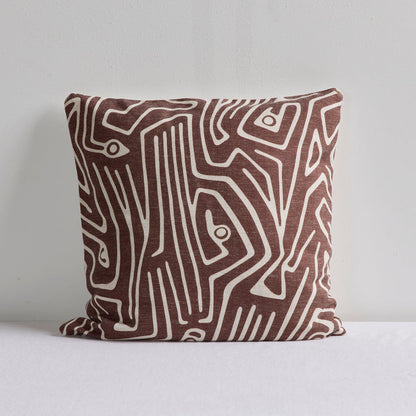 A square throw pillow with an abstract brown and cream line pattern, resting on a white surface against a light gray wall.