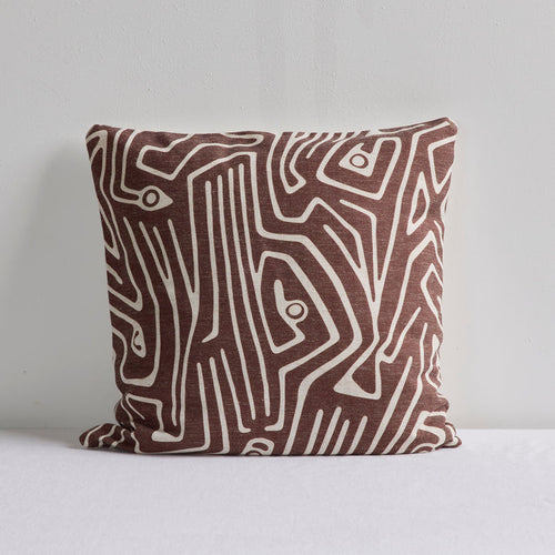 A square throw pillow with an abstract brown and cream line pattern, resting on a white surface against a light gray wall.