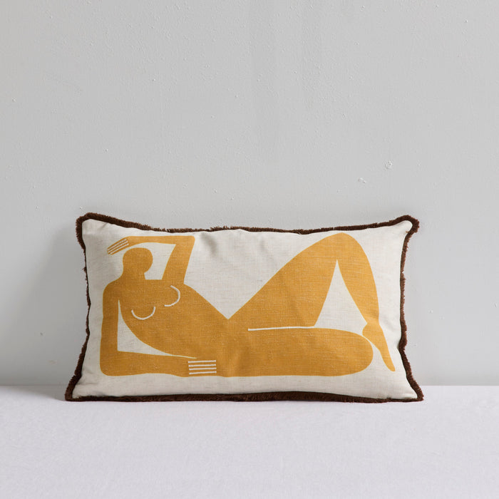 A rectangular throw pillow with a dark brown fringed edge, featuring a mustard yellow minimalist art-deco style illustration of a reclining figure on an off-white linen background.
