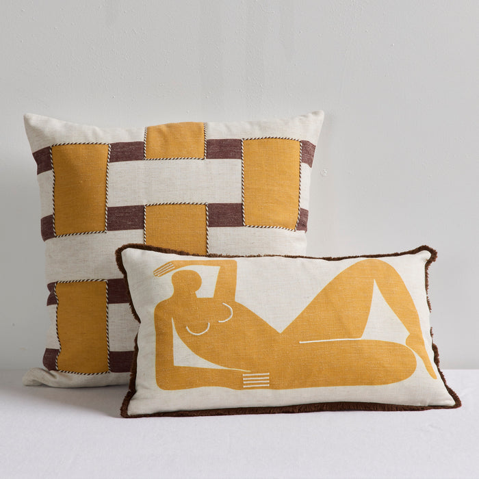 Two decorative throw pillows in a warm neutral color palette. The taller back pillow features a patchwork design of mustard yellow, cream, and dark brown.