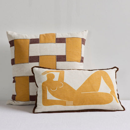 Two decorative throw pillows in a warm neutral color palette. The taller back pillow features a patchwork design of mustard yellow, cream, and dark brown.