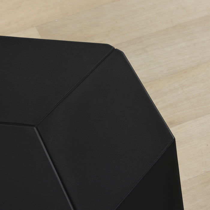 Close-up of a matte black geometric side table corner on a light wood floor.