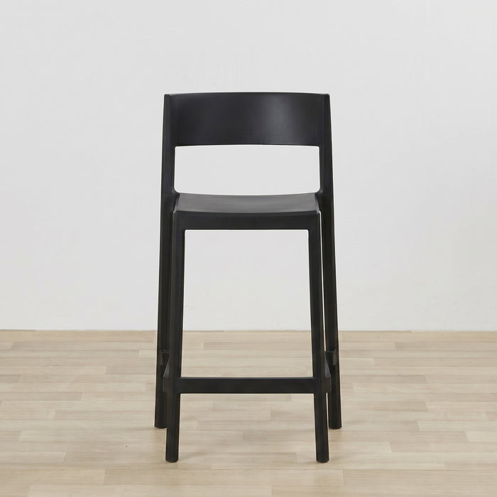 A modern black bar stool with a minimalist open-back design, shown on a light wood floor against a plain white wall.