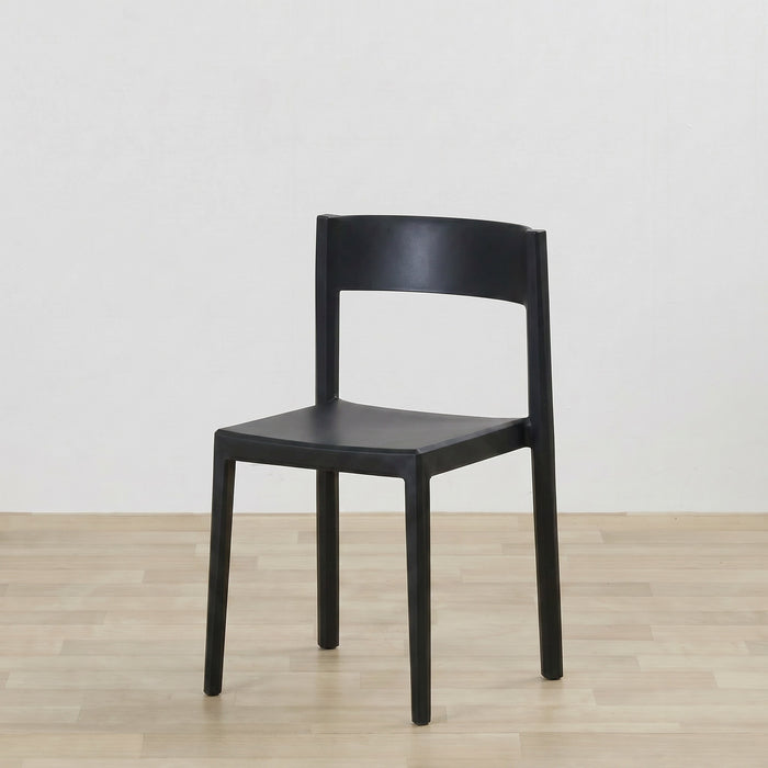 A modern black plastic dining chair with a curved backrest and four legs, shown on a light wood floor against a white wall.
