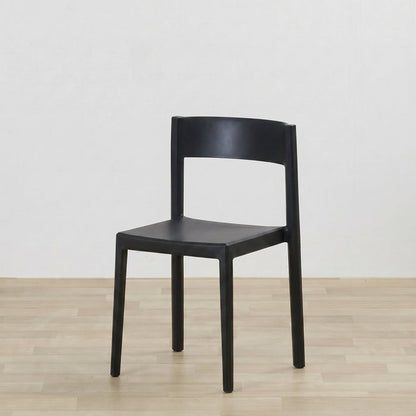 A modern black plastic dining chair with a curved backrest and four legs, shown on a light wood floor against a white wall.