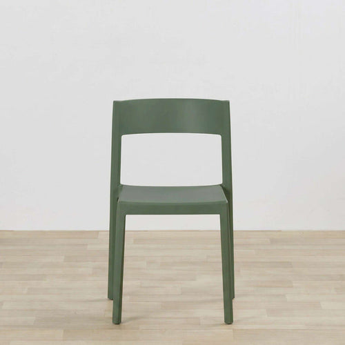 A modern molded plastic chair in a muted sage green color, positioned centrally against a white wall and light wood floor.