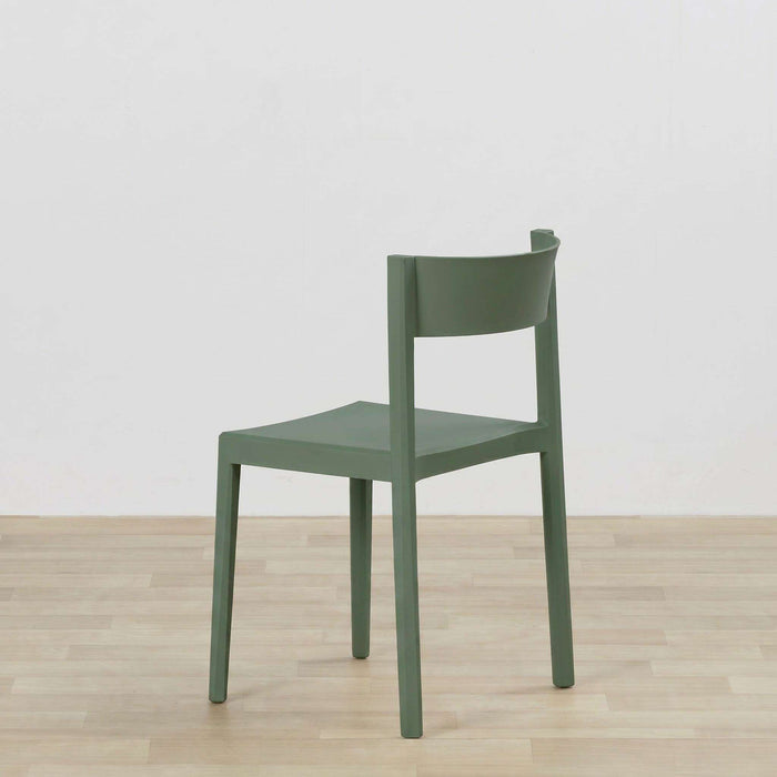 A modern molded plastic dining chair in a muted sage green color, positioned on a light wood floor against a plain white wall.