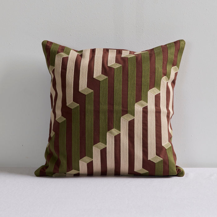 A square throw pillow with a geometric 3D-effect stripe pattern in olive green, dark brown, and cream, set against a plain light gray background.