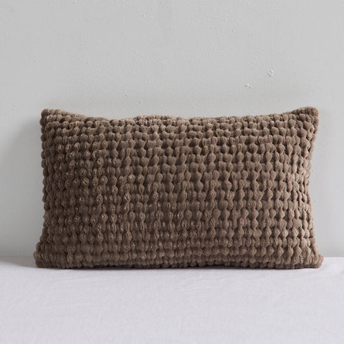 A rectangular textured throw pillow in a taupe brown bouclé fabric, resting on a white surface against a light gray wall.