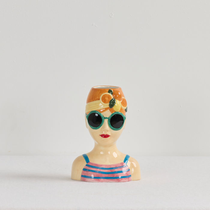 Ceramic vase shaped like a woman's head with sunglasses and a swimsuit on a light gray background