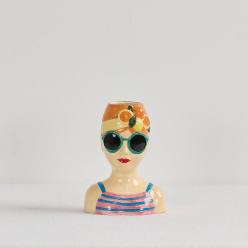 Ceramic vase shaped like a woman's head with sunglasses and a swimsuit on a light gray background